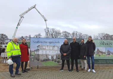 Fünf Männer und eine Frau stehen draußen vor einem Baustellenschild im EQ Businesspark Quickborn.
