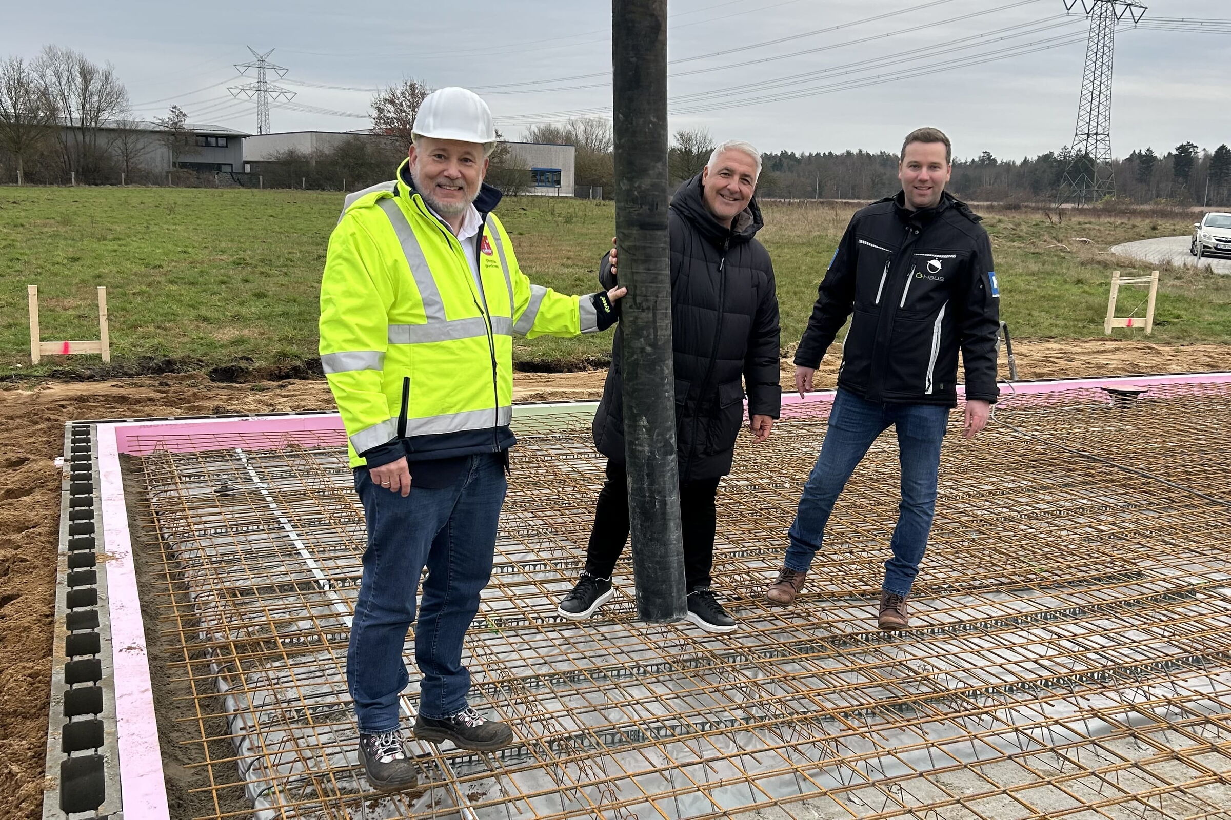 Drei Männer stehen auf einer Baustelle und leiten den Baubeginn der Betonsohle ein.
